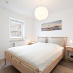 Schlafzimmer mit Holzbett, Nachttischen und Wandbild. Fenster mit Blick auf Gebäude.