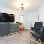 Wohnzimmer mit Fernseher, zwei Sesseln und Holzboden.