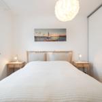 Schlafzimmer mit Bett, Nachttischen und Wandbild. Fenster und Schrank sind sichtbar.