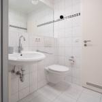 Badezimmer mit Waschbecken, Toilette und Spiegel an der Wand.