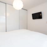 Schlafzimmer mit Bett, Schwebetüren und Wandfernseher.