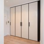 Schwebetüren-Schrank mit dunklen Rahmen und Griffen. Holzfußboden und weiße Wände.