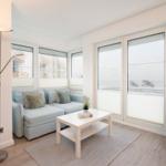 Wohnzimmer mit Sofa, Tisch und großen Fenstern mit Meerblick.