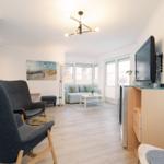 Wohnzimmer mit Sofa, Sesseln und Fernseher an der Wand