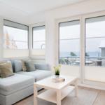 Wohnzimmer mit Sofa, Tisch und großen Fenstern zum Meer