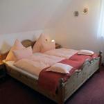 Doppelbett mit Holzrahmen, Nachttische und Fenster mit Vorhängen.