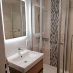 Badezimmer mit Dusche, Waschbecken und beleuchtetem Spiegel.