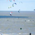 Mehrere Kitesurfer üben auf dem Meer. Einige Personen stehen am Strand.