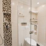 Dusche mit Mosaikwand, Toilette und integrierte Regale mit Handtüchern.