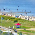 Strand mit Badegästen, Strandkörben und grünen Dünen im Hintergrund.