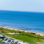 Strand mit Badegästen, Grünflächen und Campingplatz im Hintergrund.