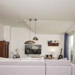 Wohnzimmer mit Sofa, Fernseher und Schwebelampen. Fenster mit blauen Vorhängen.