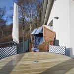 Terrasse mit Tisch, Stühlen und Strandkorb. Blick auf Wald und Hauswand.