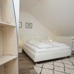 Schlafzimmer mit Dachschrägen, weißem Bett und Dachfenster. Holzregal im Vordergrund.