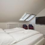 Doppelbett mit weißer Bettwäsche, zwei rote Sessel, TV und Dachfenster.