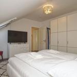 Schlafzimmer mit Doppelbett, Kleiderschrank, TV und roten Sesseln.