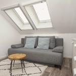 Wohnzimmer mit grauem Sofa, Holztisch und Dachfenstern.