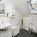 Badezimmer mit Dusche, Spiegel und Fenster. Weiße Fliesen und dunkle Bodenfliesen.