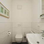 Badezimmer mit Toilette, Waschbecken und Spiegel. An der Wand hängt ein Bild mit Pflanzenmotiv.