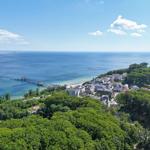 Panoramablick auf Strand, Hafen und grüne Landschaft mit Hotels und Häusern.