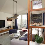 Wohnzimmer mit Sofa, Fernseher und Terrasse. Holzregal, Pflanzen und Sitzkissen.