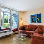 Wohnzimmer mit rotem Sofa, Glas-Tisch und großen Fenstern. Wandbilder zeigen Fische.