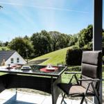Terrasse mit Tisch und Stühlen. Blick auf grüne Hügel und einen Wasserturm.