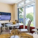 Essbereich mit Glasrundtisch, Stühlen und TV. Blick auf Garten durch große Fenster.