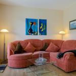 Ein Wohnzimmer mit einem roten Sofa, Glas-Tisch und Wandbildern.