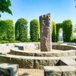 Steinmauer-Labyrinth mit zentraler Säule und grünen Bäumen im Hintergrund.