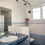 Badezimmer mit zwei Waschbecken, Spiegelschrank und Fenster. Wandfliesen mit Meeresmotiv.