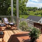 Terrasse mit Liegestühlen und Tisch, Blick auf grüne Landschaft und Haus.