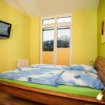 Schlafzimmer mit Doppelbett, Fernseher und Fenster mit Blick auf Außenbereich.