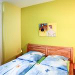 Schlafzimmer mit gelben Wänden, Bett mit blauer Bettwäsche und zwei Nachttischen.