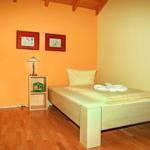 Ein Schlafzimmer mit Holzboden, Bett, Schrank und Nachttisch. Wandfarbe orange und gelb.