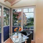 Sitzgelegenheit mit Glas-Tisch und Blumen vor großem Fenster mit Blick auf Gebäude und Grün.