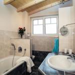 Bad mit Badewanne, Waschbecken und Fenster. Holzdecke und rote Rosen.