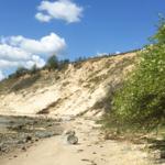 Strand mit sandigen Dünen und blauem Himmel mit weißen Wolken.