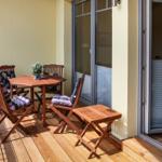 Terrasse mit Holztisch und vier Stühlen mit Kissen, gläserne Schiebetüren und Holzdielen.
