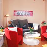 Ein Wohnzimmer mit roten Sesseln, grauem Sofa und runden Tisch. An der Wand hängt ein Bild.