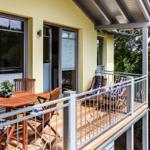 Terrasse mit Holztisch, Stühlen und Liegestühlen. Blick in den Wald.