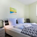 Ein Schlafzimmer mit Bett, Nachttisch und Fenster. Wandbild und Handtücher sind sichtbar.