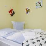 Ein Bett mit gestreifter Bettwäsche und einem Sternenbezug. An den Wänden hängen farbige Bilder.