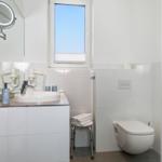 Badezimmer mit Dusche, Toilette, Waschbecken und Fenster.