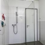 Dusche mit Glaswand, Duschbrause und Handbrause, Wandheizung und Handtuchhalter.