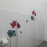 Duschbereich mit weißen Fliesen und bunten Blumenmotiven an der Wand.