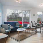 Wohn- und Essbereich mit Sofa, Sesseln und Tisch. Durchgänge zu Küche und Balkon.