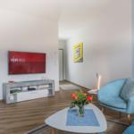 Wohnzimmer mit TV, Sitzgelegenheiten und dekorativen Wandbildern.