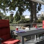 Terrasse mit Tisch und zwei roten Stühlen. Blick auf einen Wasserturm und grüne Bäume.