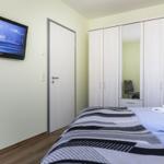 Schlafzimmer mit Bett, Kleiderschrank und Wandfernseher.